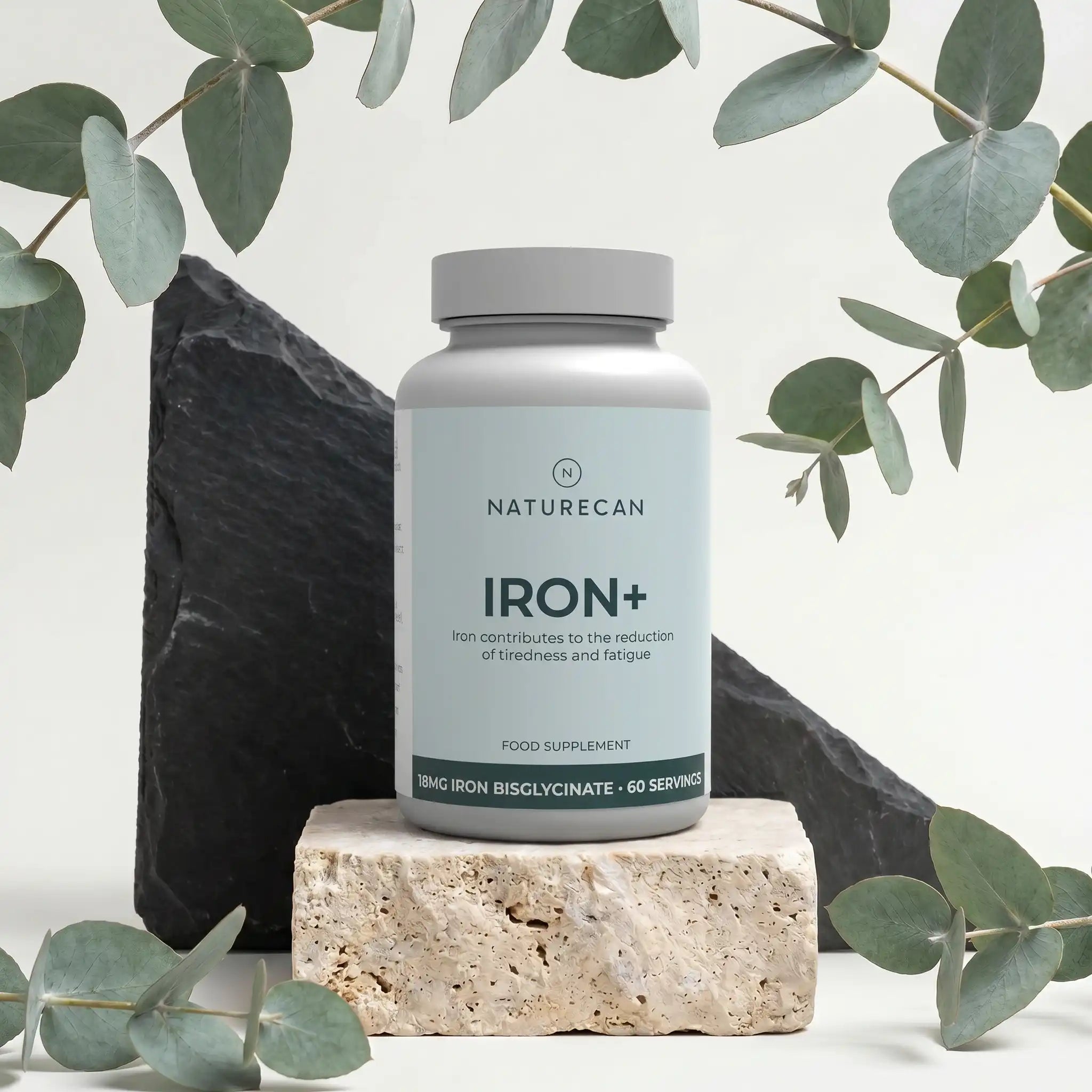 Żelazo w kapsułkach Naturecan Iron+ z 18 mg bisglicynianu żelaza, 60 porcji, na dekoracyjnym tle z liśćmi.