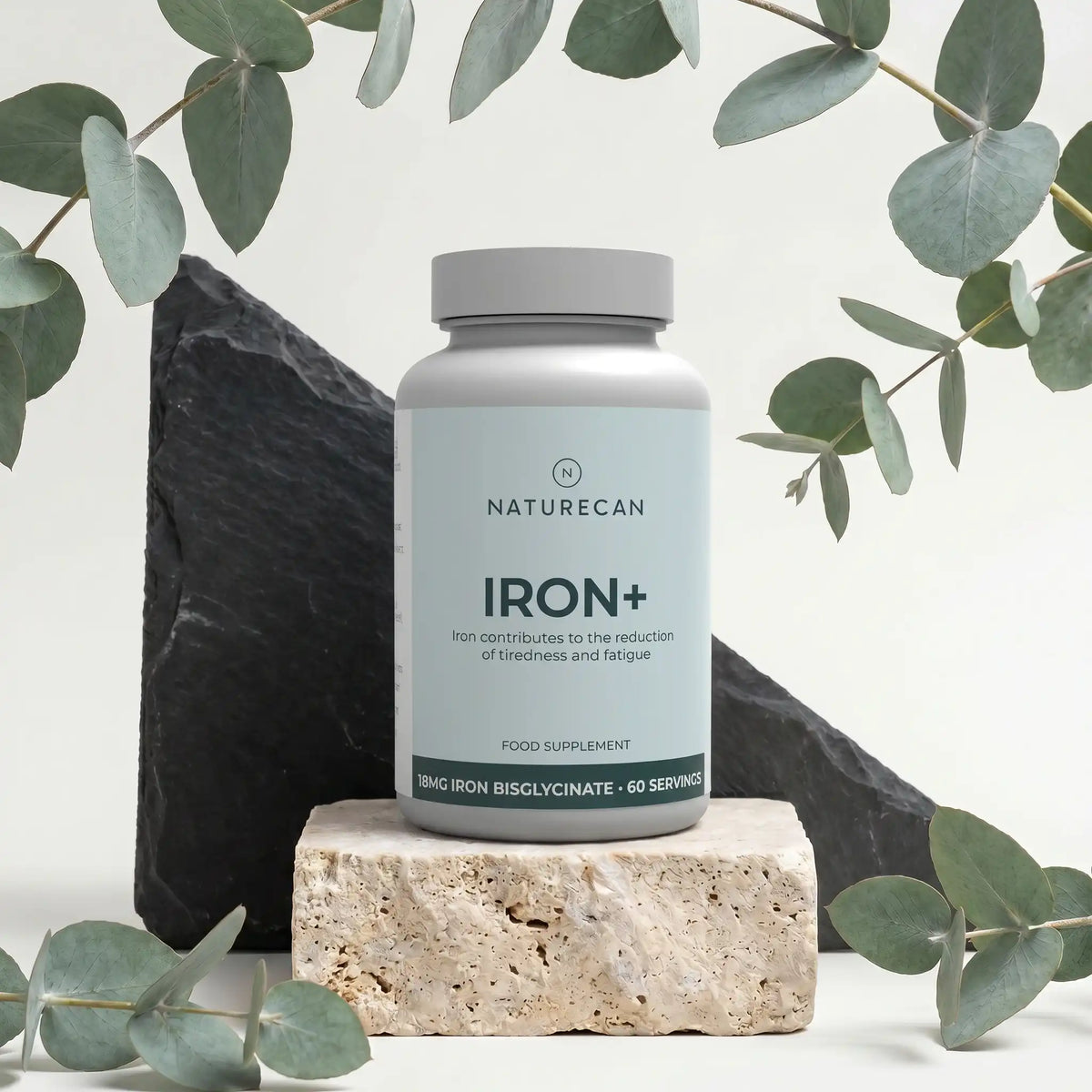 Żelazo w kapsułkach Naturecan Iron+ z 18 mg bisglicynianu żelaza, 60 porcji, na dekoracyjnym tle z liśćmi.