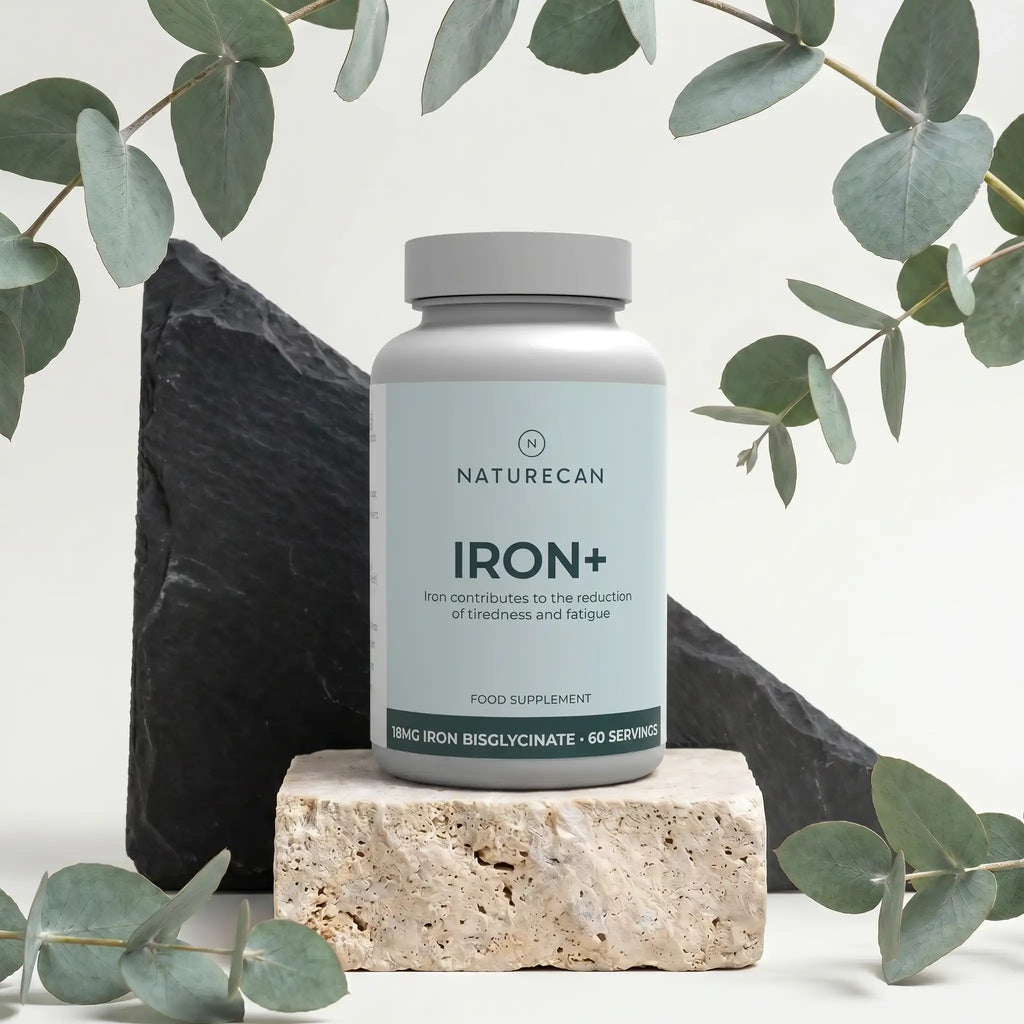 Żelazo w kapsułkach Naturecan Iron+ z 18 mg bisglicynianu żelaza, 60 porcji, na dekoracyjnym tle z liśćmi.